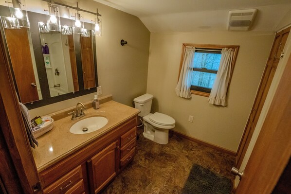 A bathroom with a sink, mirror, vanity, toilet, and a window with curtains.
