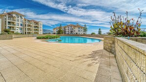 Una piscina, cielo sereno, un edificio con balconi e un'area verde curata.