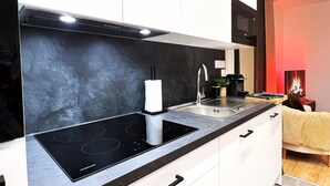 Eine moderne Küche mit einem schwarzen Induktionskochfeld, einer Edelstahl-Spüle und weißen Schränken.