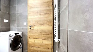 Ein Waschraum mit einer weißen Waschmaschine, einer Holztür und einem weißen Heizkörper.
