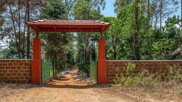 Una pérgola roja con un sendero de tierra que la atraviesa, rodeada de árboles y un muro de ladrillo.