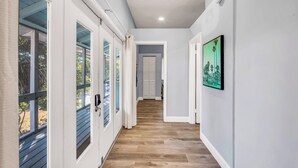A hallway with wooden flooring, white walls, and a door leading to a room with a view of palm trees. - Seahorse Suites #4. A Perfect Beach Getaway! (Sanibel)
