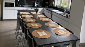 A modern kitchen with white cabinets, a black countertop, and a dining area with a long table set for six. - Comfortable house for 12 p in rustival neighborhoud (BORGLOON)