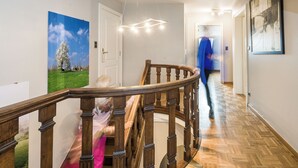 A wooden staircase with a handrail, a ceiling light fixture, and a person walking down the hallway. - Comfortable house for 12 p in rustival neighborhoud (BORGLOON)