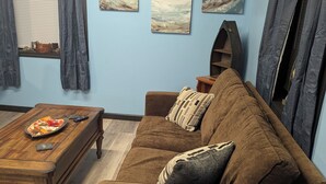 Un salon avec un canapé marron, une table basse en bois et des œuvres d’art accrochées aux murs.