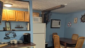 Une cuisine compacte avec des meubles en bois, un réfrigérateur blanc, un four à micro-ondes et une machine à café. On y trouve une table à manger avec des chaises et, en dessous, un petit meuble en bois.