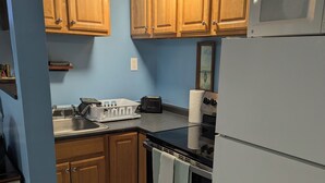 Une cuisine avec des meubles de rangement en bois, une cuisinière noire, un réfrigérateur blanc et un évier.