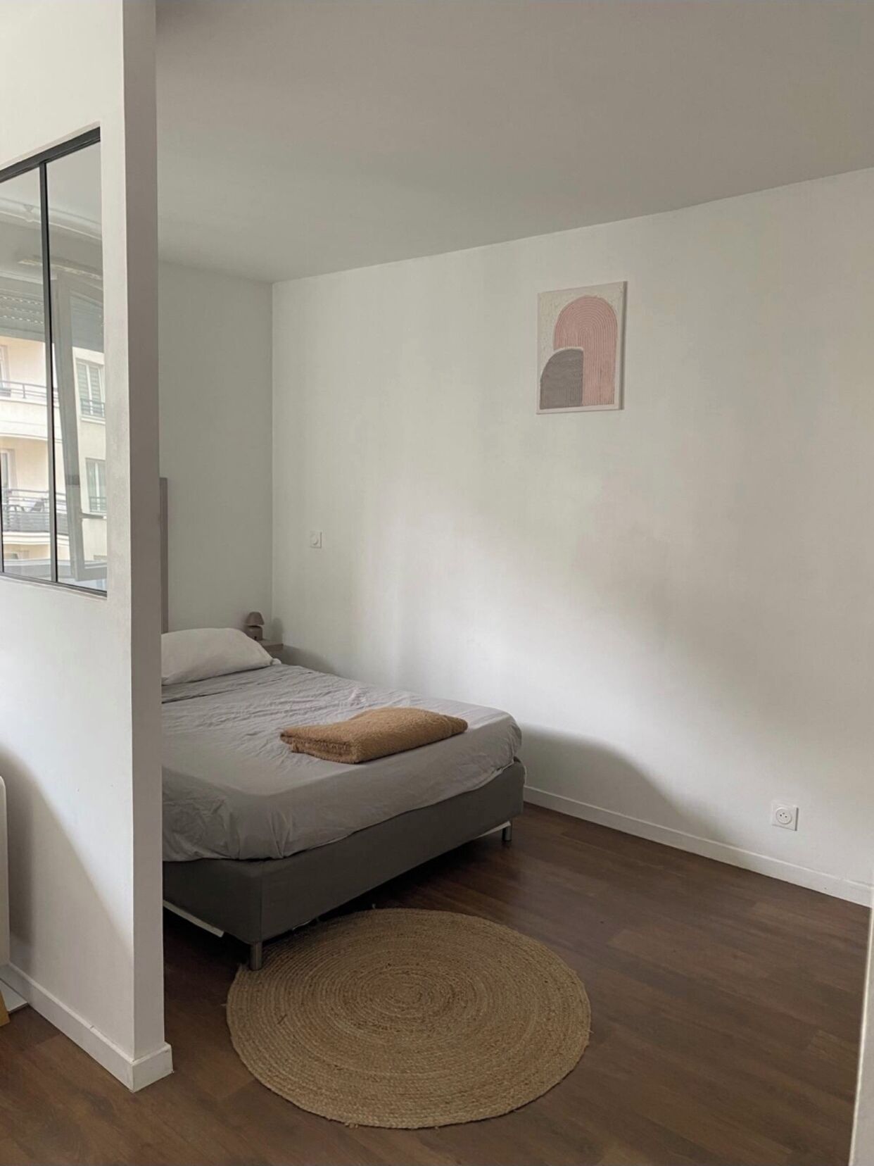 A bedroom with a bed, a round woven rug, and a wall-mounted artwork.