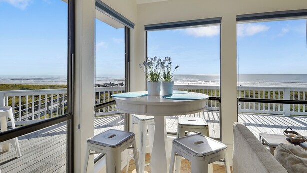 A balcony with a white table and chairs, a potted plant, and a view of the ocean.