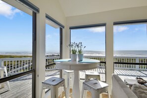 Un balcon avec une table et des chaises blanches, une plante en pot et une vue sur l’océan.