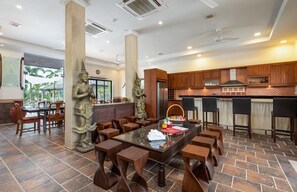 Un amplio comedor con una mesa central, rodeada de sillas de madera y un pilar de piedra con una estatua.