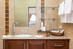 Un baño con lavamanos de encimera de granito, un espejo grande y un estante de vidrio con artículos de aseo.