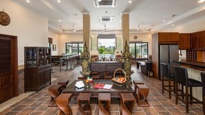A spacious dining area with a long table and chairs, a bar area with wooden cabinets, and a view of the outdoors through large windows. - Sahaswara Luxury Villa Pattaya (Bang Lamung)