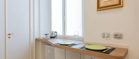 Een kleine keuken met een ingebouwd raam, een radiator, een klein krukje en een lijst met een foto aan de muur.