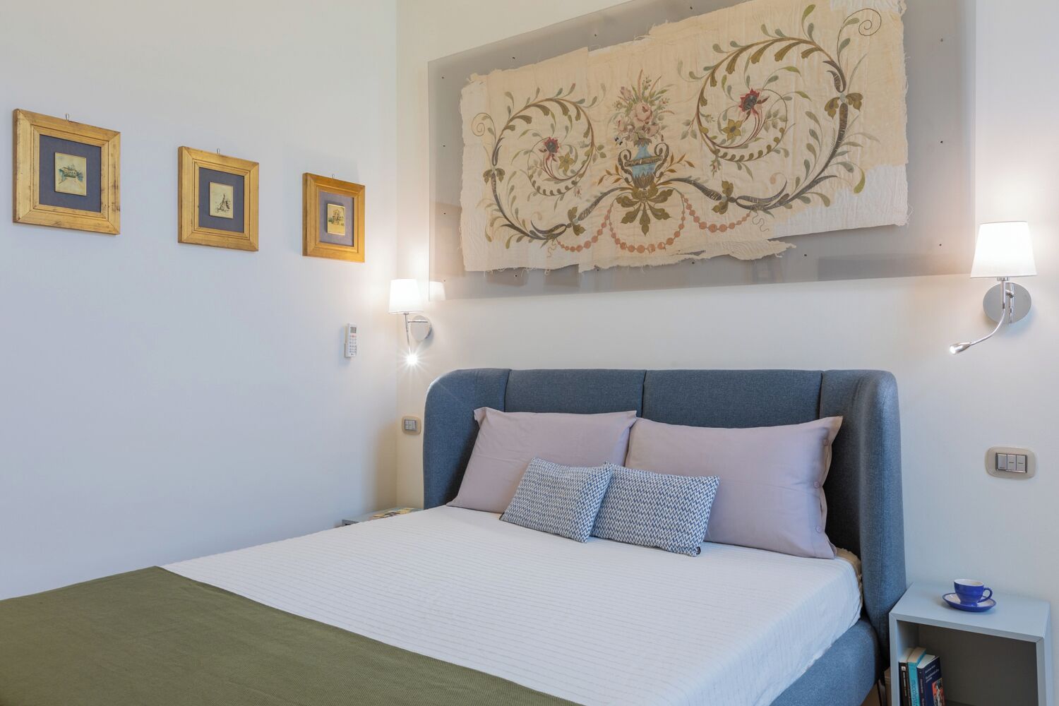 Un dormitorio con una cama, una mesita de noche, una lámpara y tres cuadros en la pared.
