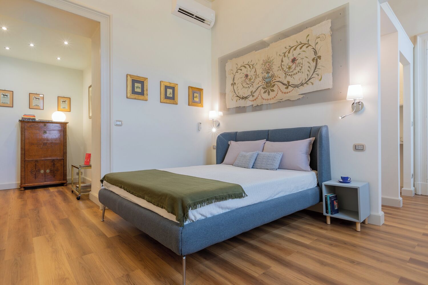 A bedroom with a bed, a dresser, a nightstand, and wall-mounted lights.