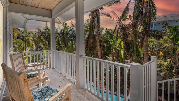 A wooden deck with a ceiling fan, white railings, and a view of a swimming pool surrounded by tropical vegetation. - Anna Maria Home with Pool and Rooftop Deck! 5-min Walk to Beach - Coconut Breeze (Anna Maria)
