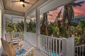 A wooden deck with a ceiling fan, white railings, and a view of a swimming pool surrounded by tropical vegetation. - Anna Maria Home with Pool and Rooftop Deck! 5-min Walk to Beach - Coconut Breeze (Anna Maria)