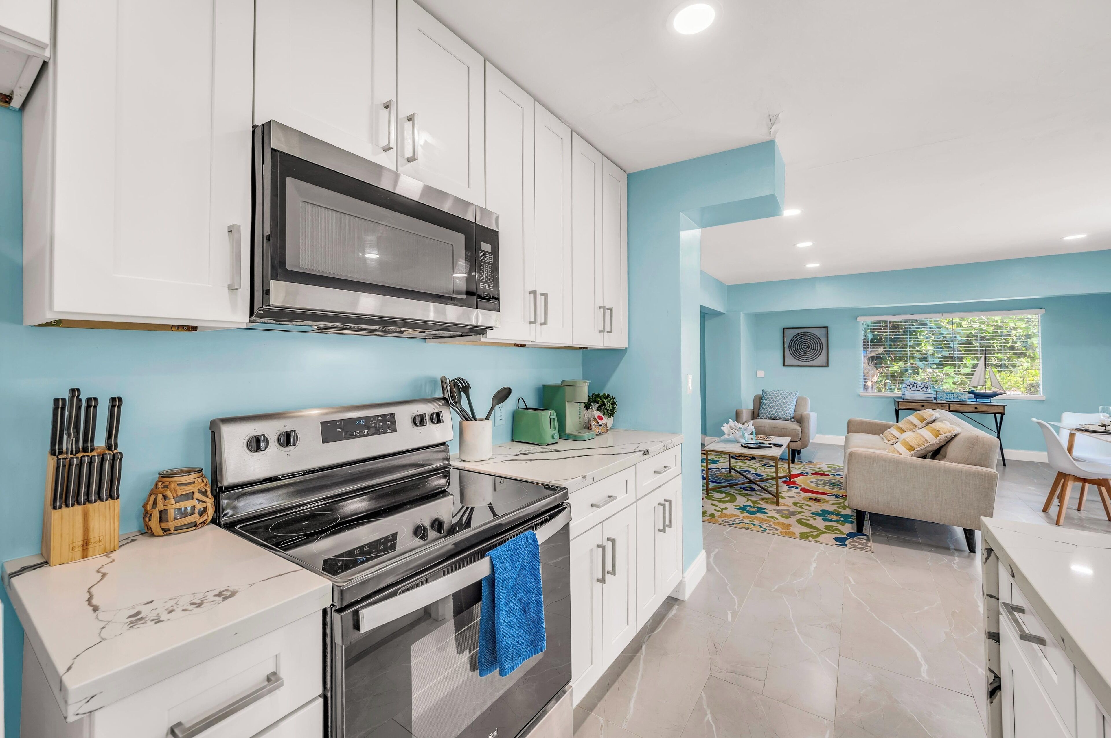 A modern kitchen with white cabinets, stainless steel appliances, and a blue accent wall.