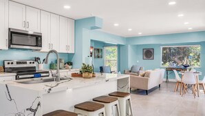 Una cucina moderna con mobili bianchi, un'isola grande con sgabelli e un'area pranzo con tavolo e sedie.