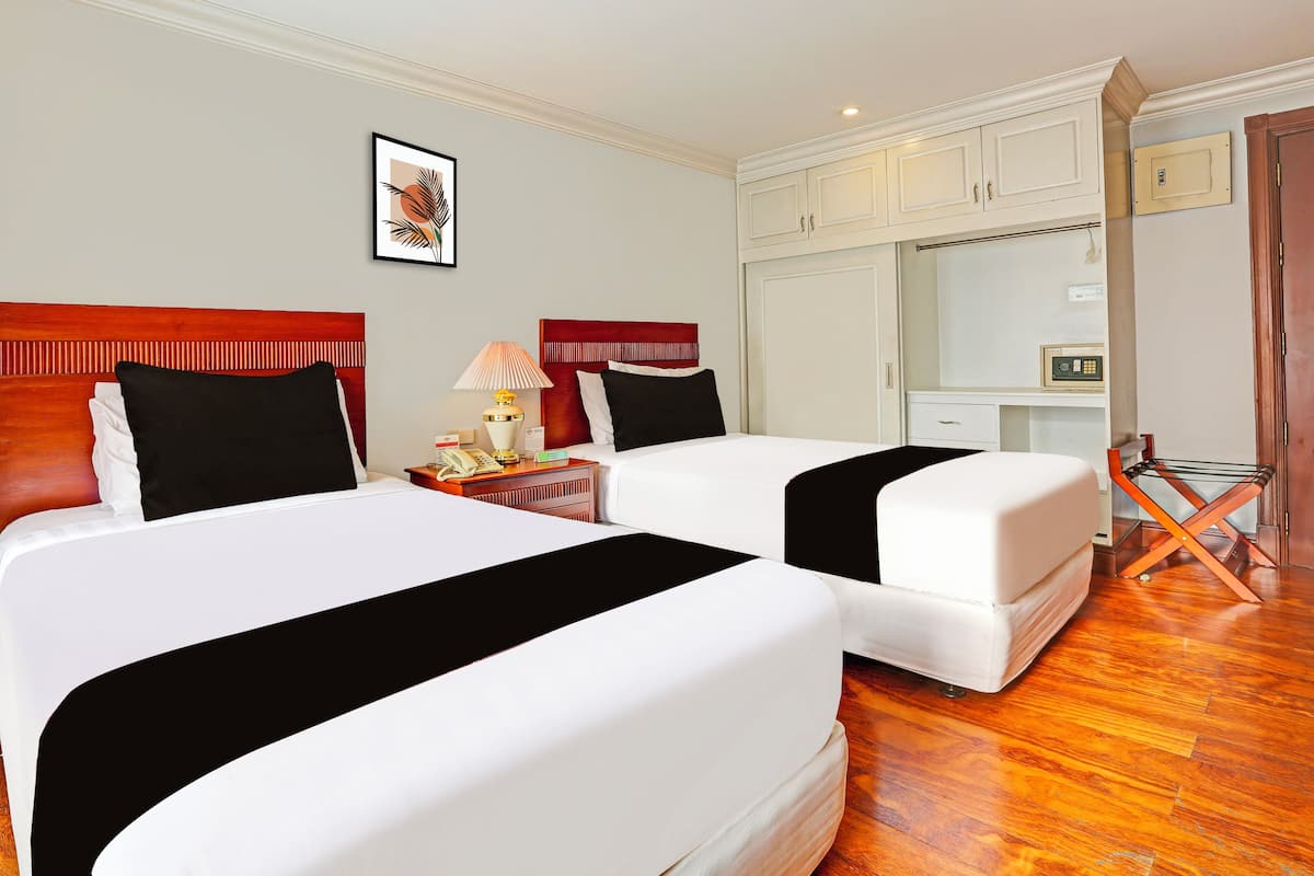 A hotel room with two beds, a desk, a chair, a lamp, and a wardrobe.