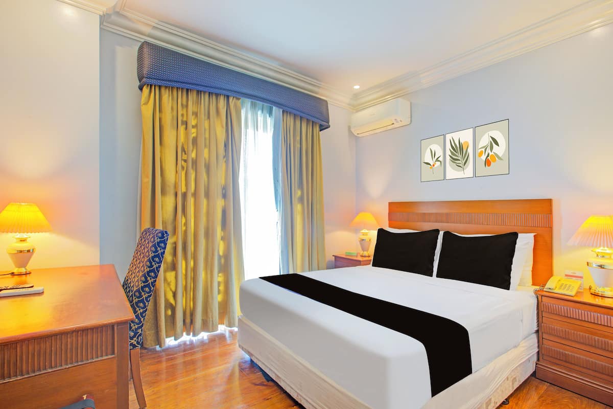 A hotel room with a large bed, a desk with a lamp, a chair, and a nightstand with a lamp.