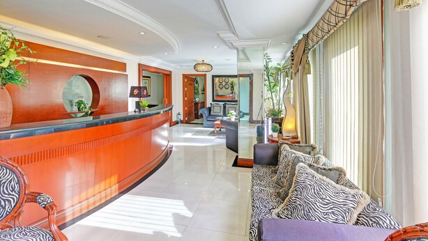 A hotel lobby with a curved reception desk, a seating area with patterned sofas, and a large window with curtains. - Townhouse Oak VIP Suites, Evangelista Makati Manila (Makati)