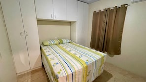 Et soveværelse med seng, garderobe og gardiner.