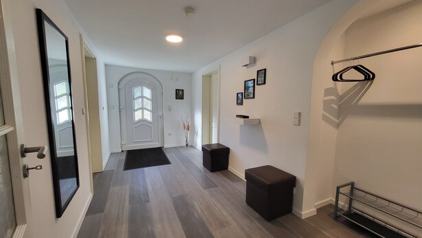 A hallway with a door, a bench, a shelf with pictures, and a radiator.
