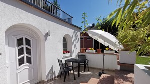 A patio with a table and chairs, a white door, and potted plants.