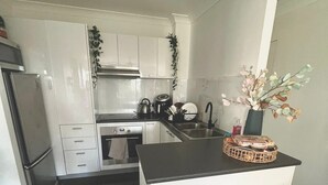 Una cocina moderna con armarios blancos, encimera negra y una pequeña isla con dos taburetes.