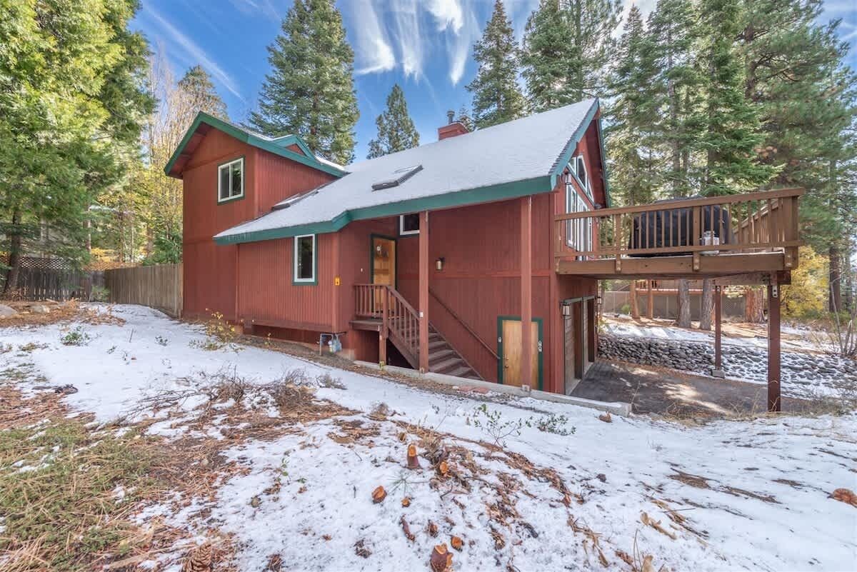 Une cabane rouge avec un toit vert, une terrasse en bois et un escalier menant à un deuxième niveau.