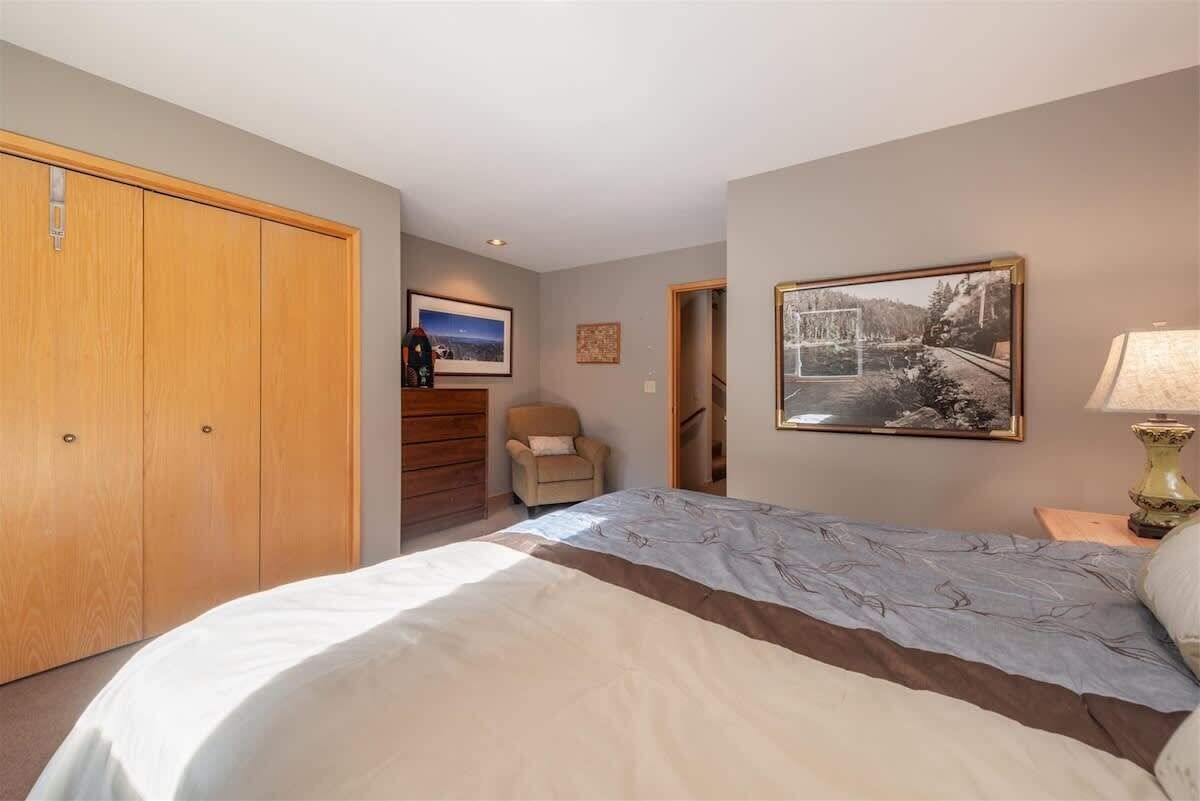 A bedroom with a bed, a wooden wardrobe, a chair, and a framed picture on the wall.