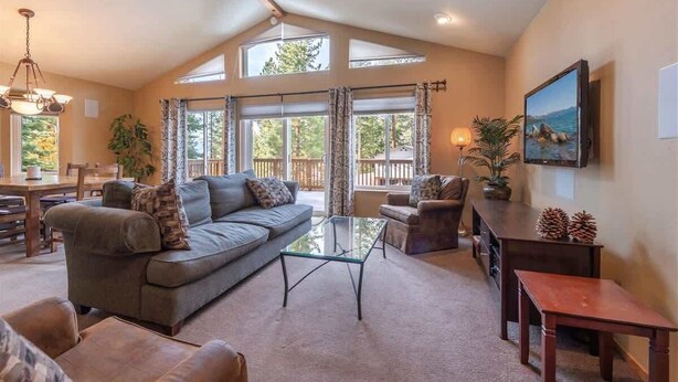 A spacious living room with a large sofa, a glass coffee table, and a television mounted on the wall. - The Jay Chalet (Tahoe City)