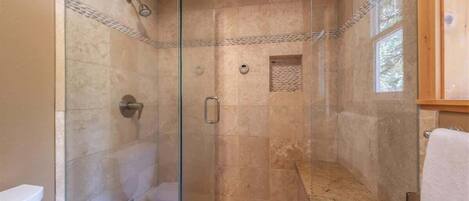 A glass-enclosed shower with a stone floor, a small window, and a towel rack.