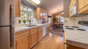 A kitchen with wooden cabinets, a stainless steel refrigerator, a white stove, and a dining area with a table and chairs. - The Jay Chalet (Tahoe City)