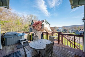 A wooden deck with a table and chairs, a hot tub, and a view of a residential area with houses and trees.