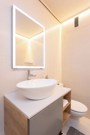 Un baño moderno con un lavamanos blanco, un espejo y un inodoro.