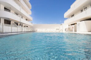 Una piscina con superficie de agua azul cristalina, rodeada por fachadas de edificios blancos con balcones.