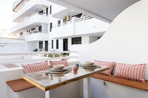 Un comedor con una mesa de vidrio, paredes blancas y un balcón con vistas a un edificio.