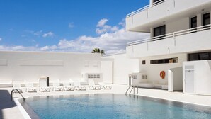 Une piscine avec des chaises longues, un bâtiment blanc et un ciel dégagé.