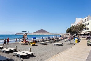 Una playa con tumbonas, una torre de salvavidas y una vista despejada del océano y una montaña al fondo.