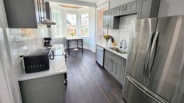 A modern kitchen with stainless steel appliances, a dining area with a table and chairs, and a view of the outside through large windows. - Luxurious Loft Inspired Living (Montgomery)
