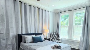 A bedroom with a bed, a ceiling fan, a window with curtains, and a chair. - Luxurious Loft Inspired Living (Montgomery)