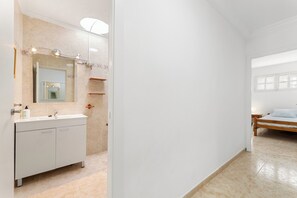 Un baño moderno con tocador blanco, un espejo grande y zona de ducha.