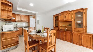 Een keuken met houten kastjes, een eettafel, stoelen, een magnetron en een spoelbak.