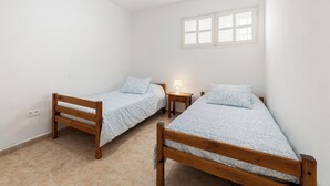 Een kleine, schone kamer met twee houten bedden, een klein nachtkastje met een lamp en een raam met zonwering.