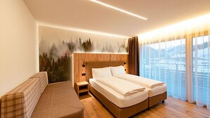 Une chambre d’hôtel avec un lit, un banc et une vue sur un paysage enneigé, visible à travers de grandes fenêtres.