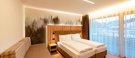 A hotel room with a bed, a bench, and a view of a snowy landscape through large windows.
