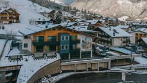 Une ville de montagne enneigée, avec des bâtiments en bois et un hôtel imposant orné d’une fresque murale.